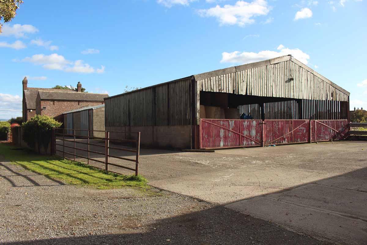 Photo of a farm for sale with external agricultural buildings and surrounding fields.